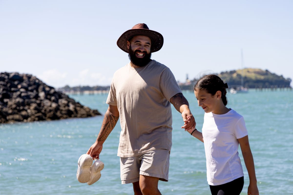 A Kiwi man walks at the beach with his daughter