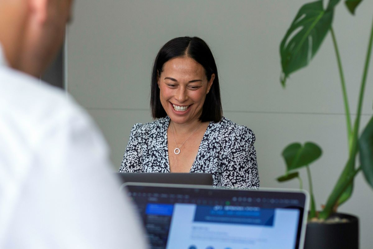 A smiling woman sits at her laptop.