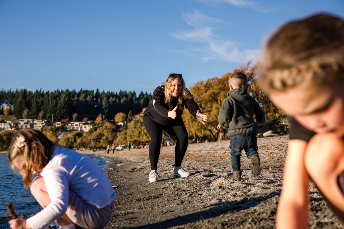 A woman plays with her children on the shore.