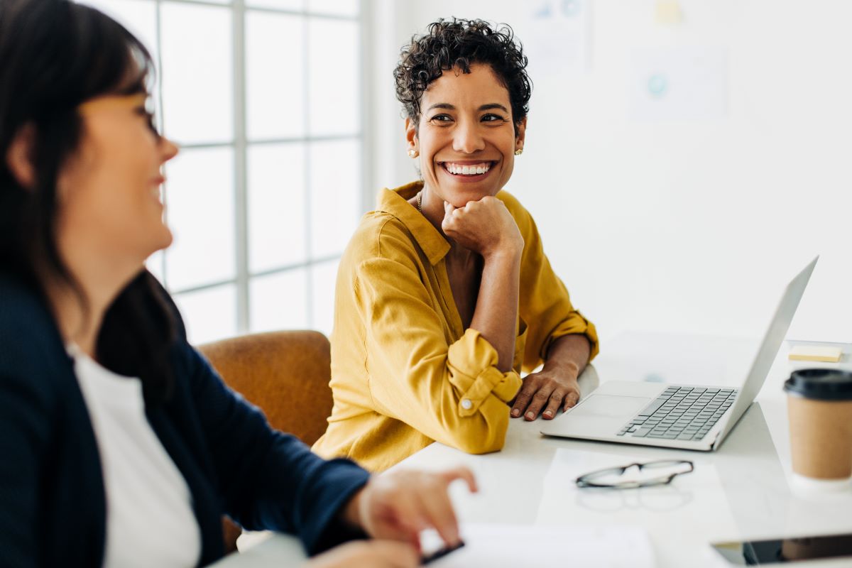 Two smiling coworkers sit at a desk