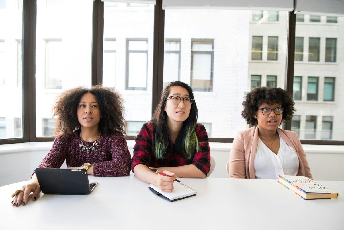 Three female professionals watch a presentation.
