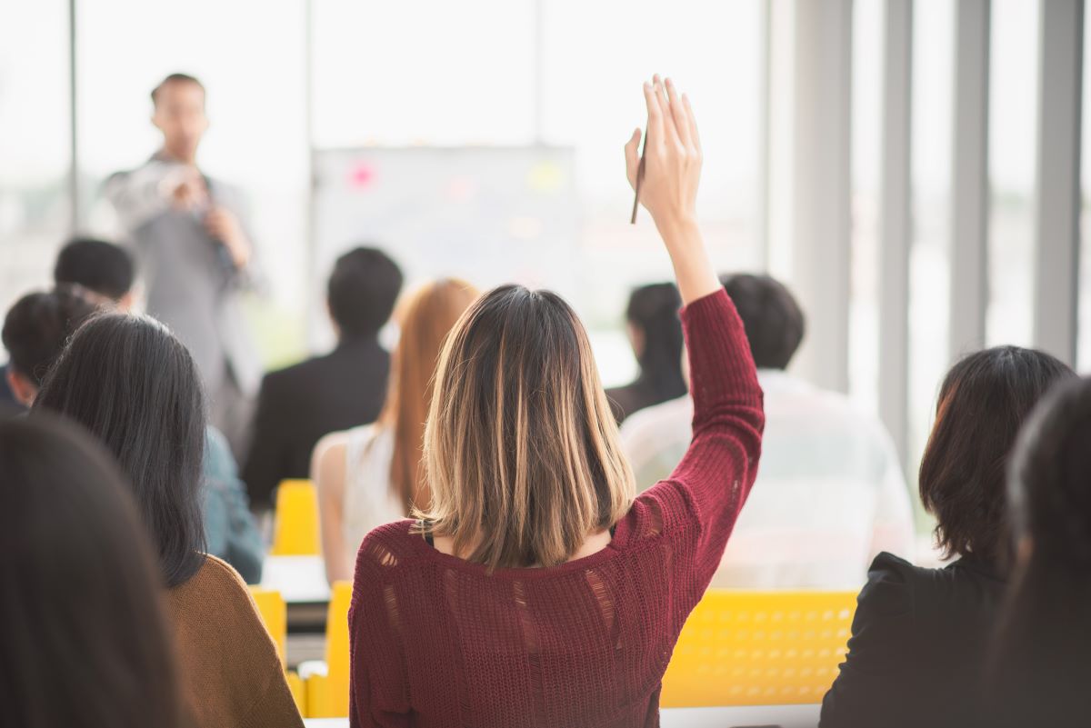 A woman raises her hand in a work meeting.