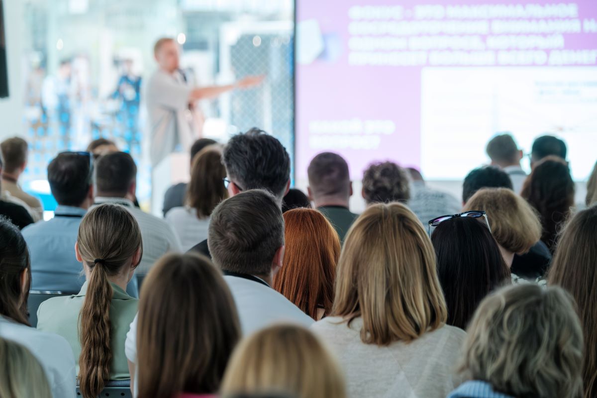 A large group of coworkers listen to a man presenting.