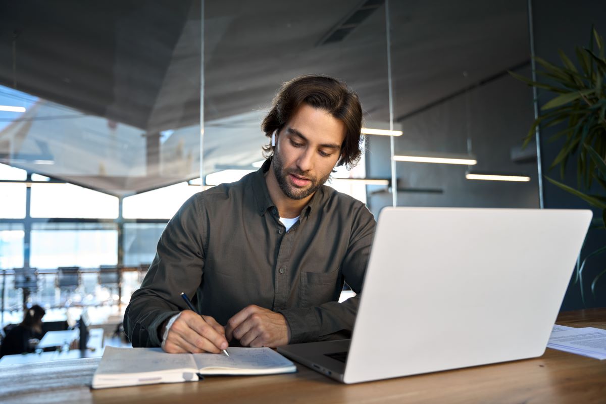A man works on a notebook and laptop.