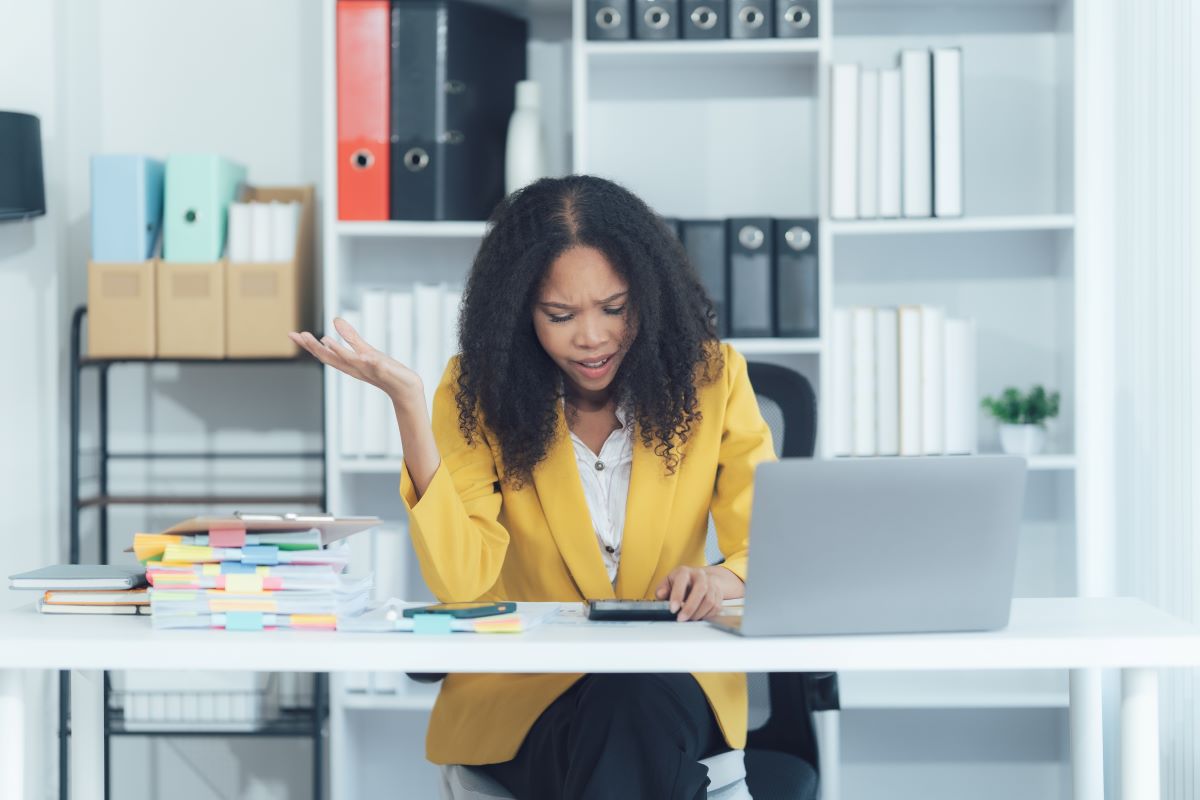 A stressed woman at work sits at her laptop.